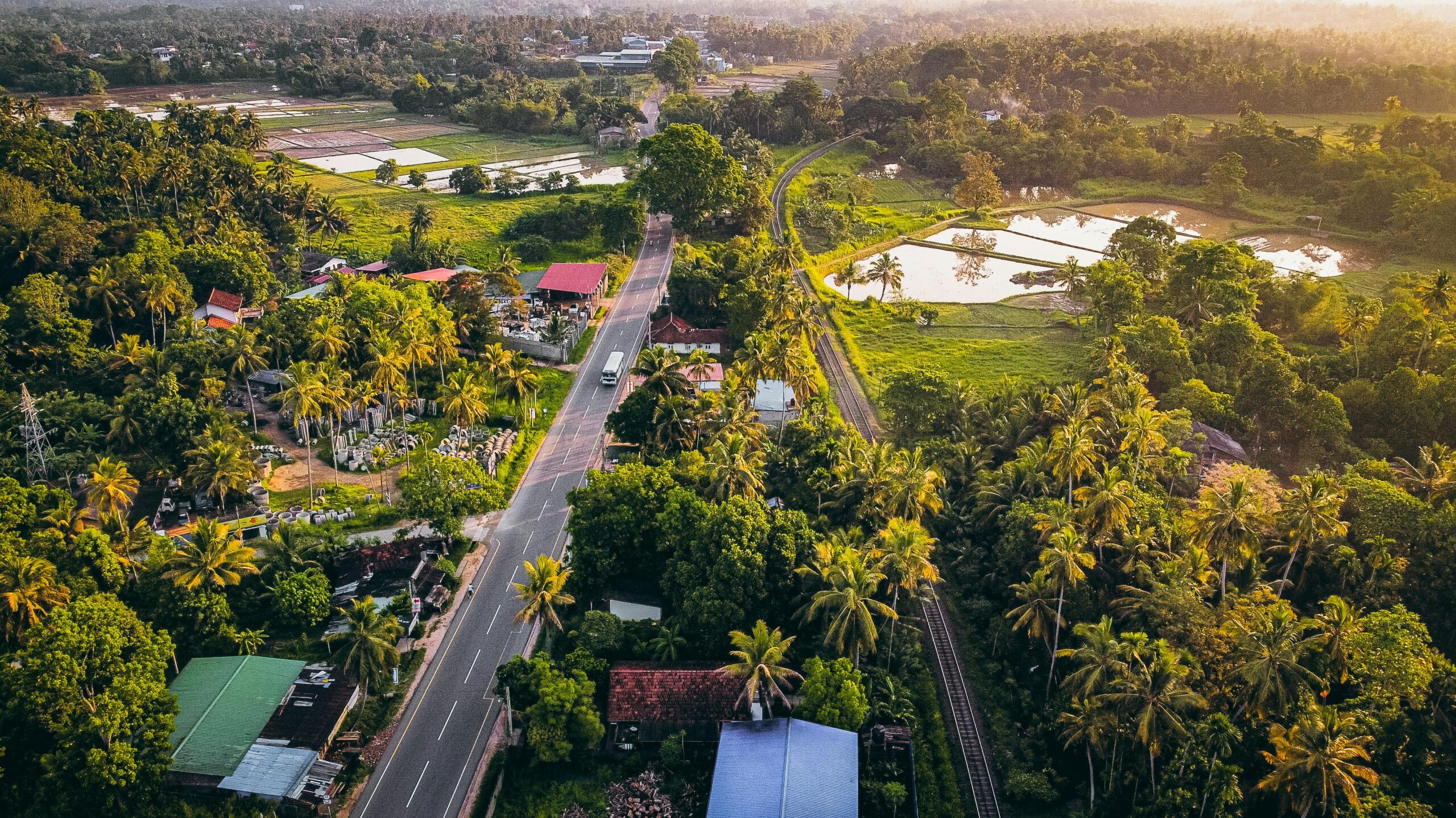 Aerial photograph capturing a lush green countryside with a road and railway at sunset.